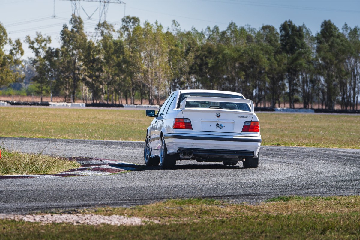 BMW E36 328i de tracción trasera para drift tomando una curva, vista trasera